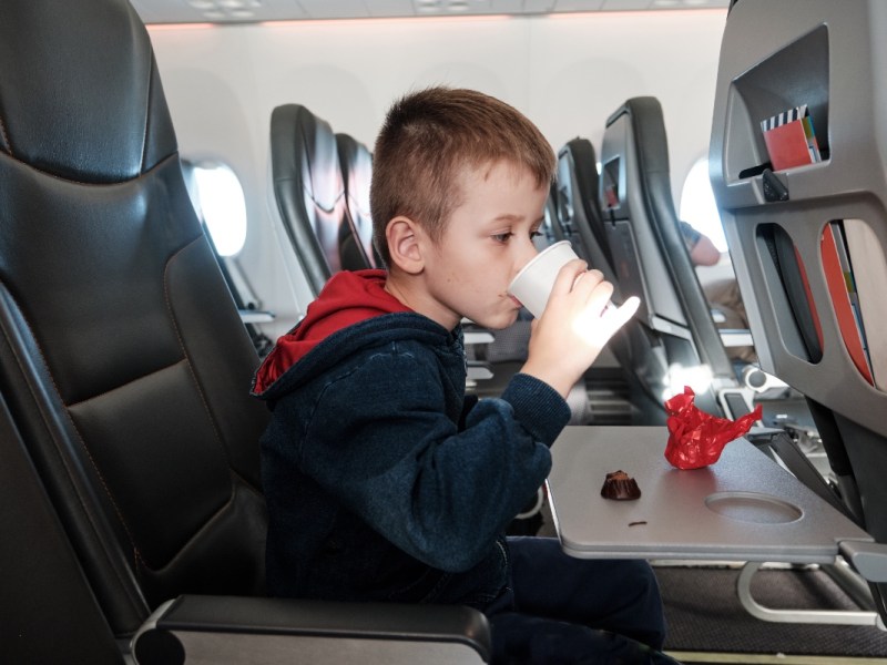 Ein blonder Junge trinkt in einem Flugzeug aus einem Becher.