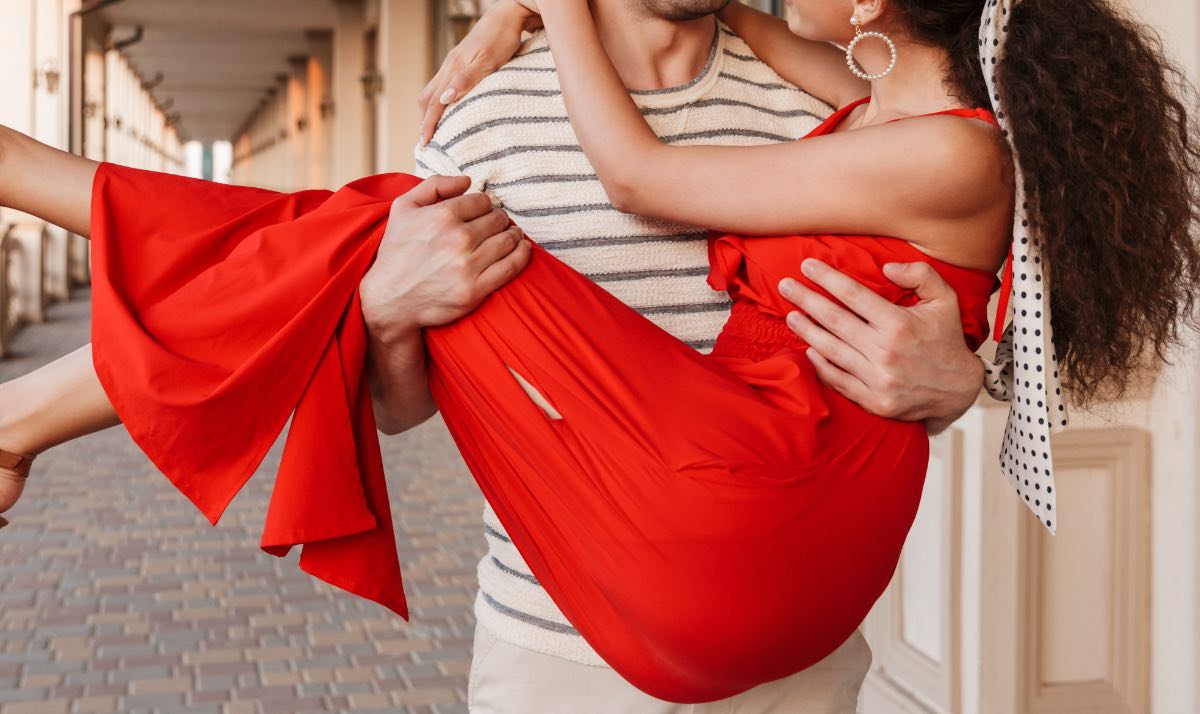 Ein Bild von einem jungen Mann, der seine Frau, die ein rotes Kleid trÃ¤gt, auf HÃ¤nden trÃ¤gt.