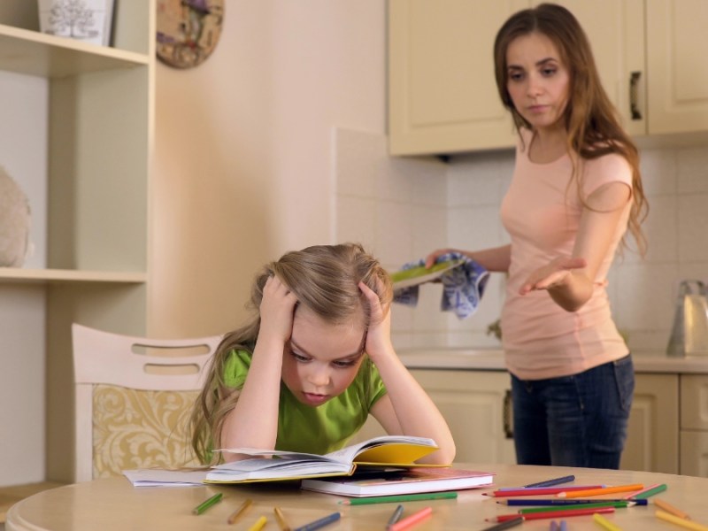 Eine junge Mutter schimpft mit ihrer jungen Tochter, die an ihren Hausaufgaben sitzt.