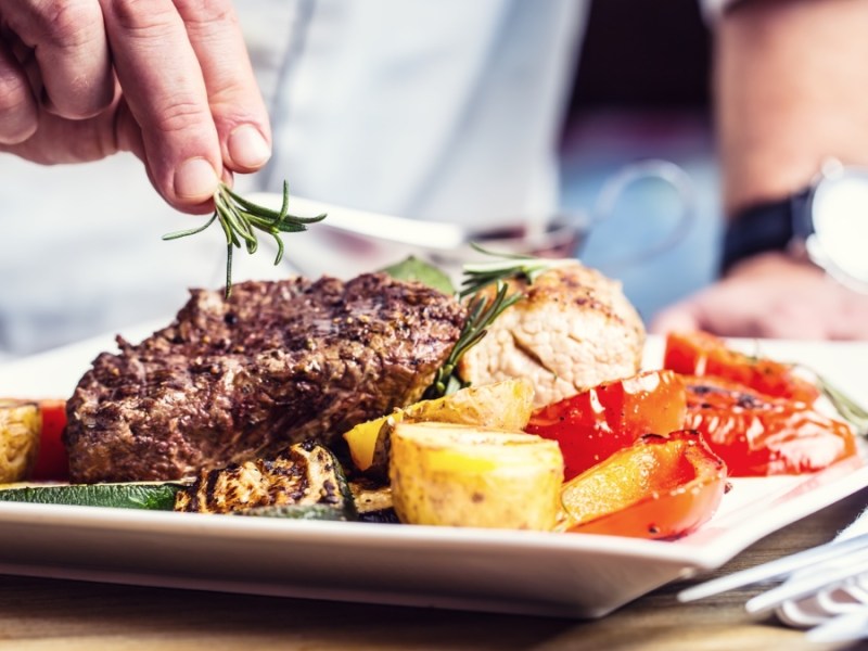 Ein Koch steht vor einem Teller mit Steak und Gemüse.