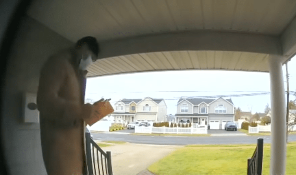 Eine Sicherheitskamera filmt einen Mann mit Maske vor einem Haus.