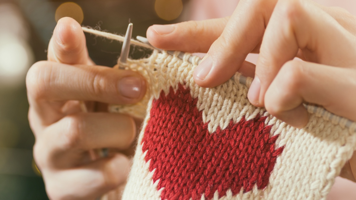 Frau strickt das rote Herz für ihren Liebsten.