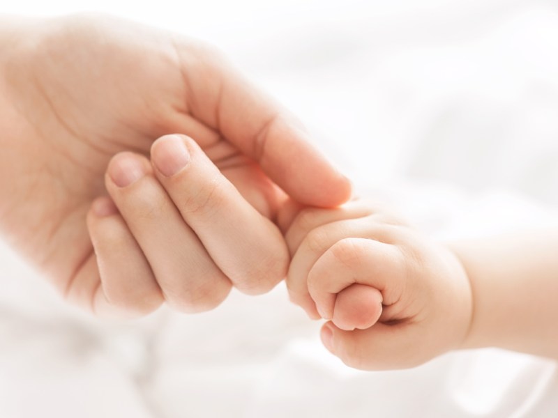 Ein Baby umfasst den Finger seine Mutter mit der Hand.