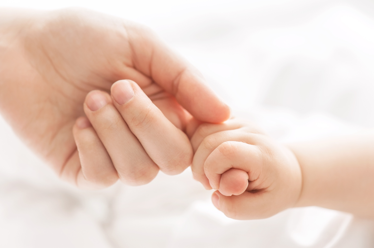 Ein Baby umfasst den Finger seine Mutter mit der Hand.