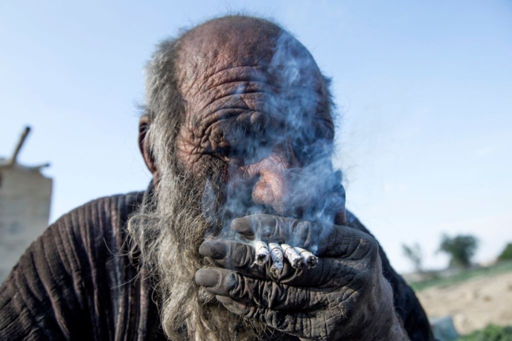 Ein alter Mann mit schmutzigem Gesicht raucht mehrere Zigaretten auf einmal.