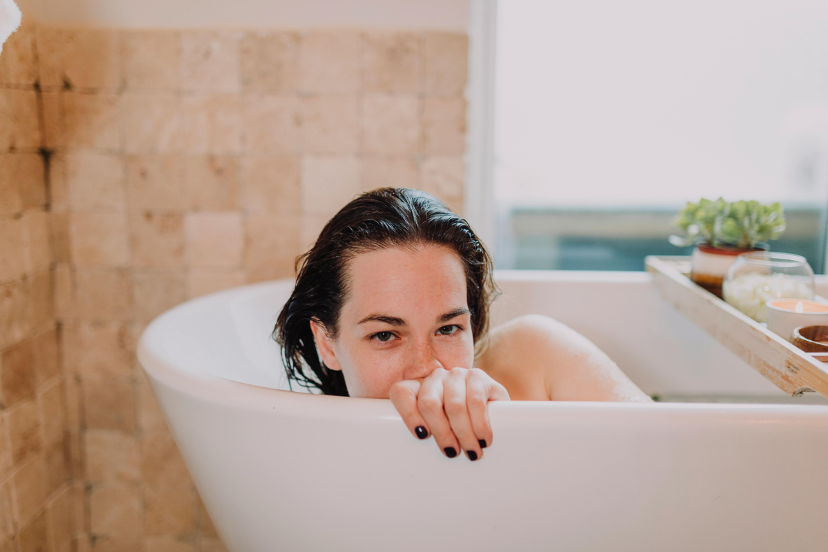 Eine junge Frau liegt in einer Badewanne und schaut über den Wannenrand.