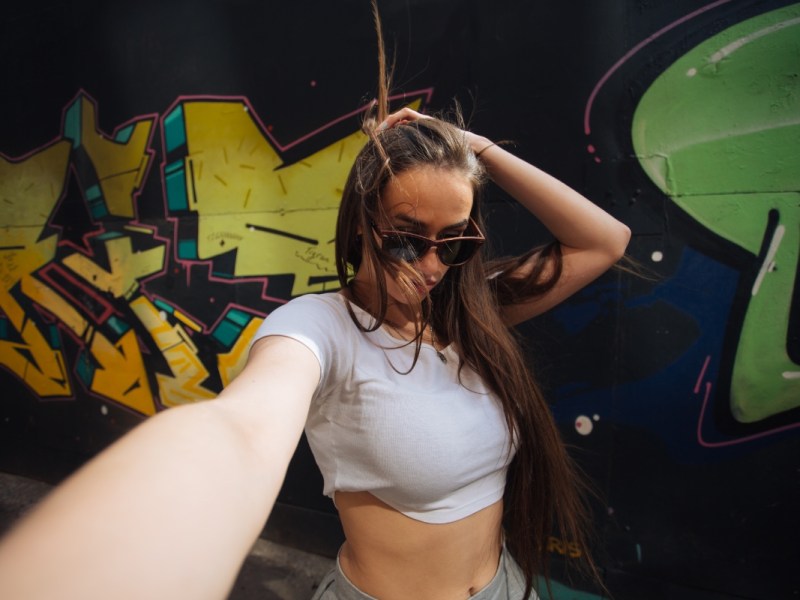 Eine junge Frau macht ein Selfie vor einem Graffiti.