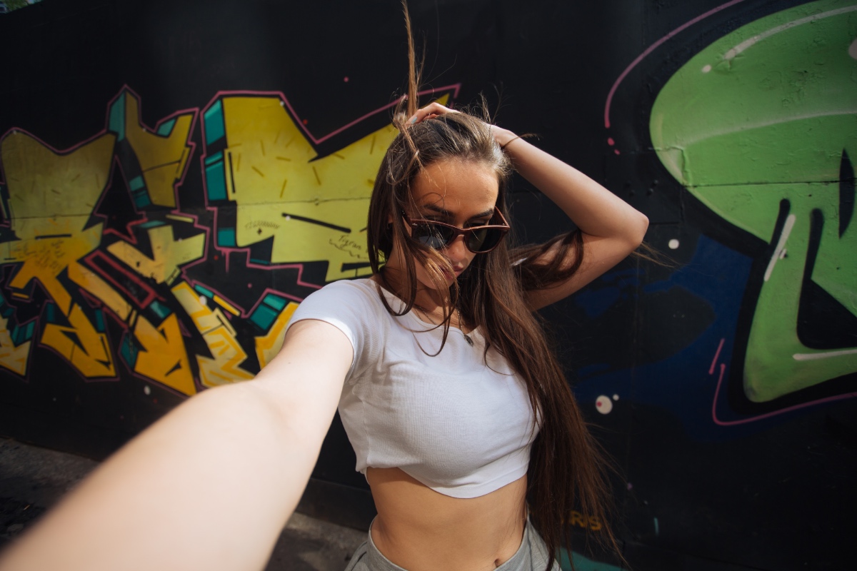 Eine junge Frau macht ein Selfie vor einem Graffiti.
