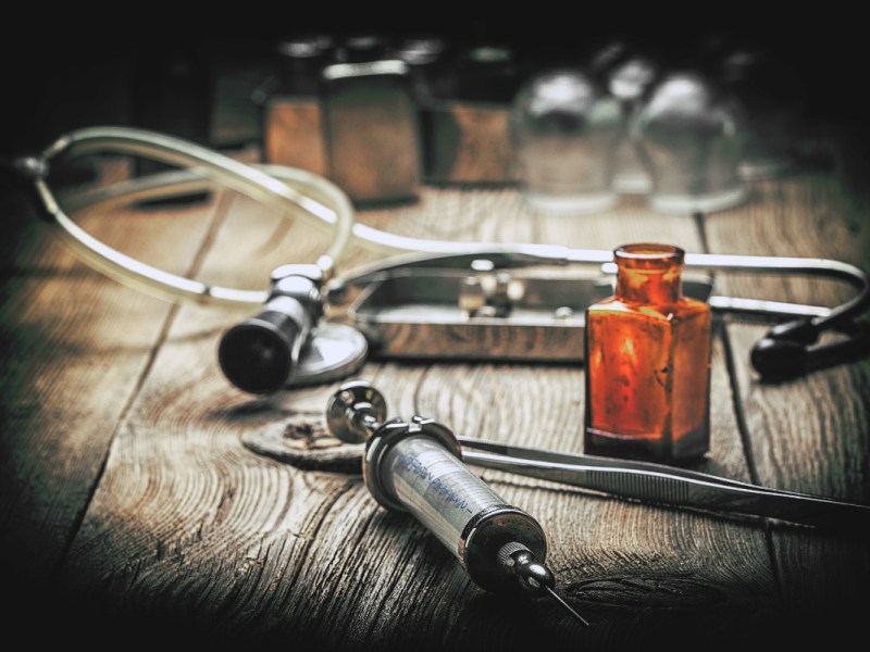 Historisches Medizin-Equipment: Eine alte Spritze, ein Stethoskop und eine Flasche auf einem Tisch.