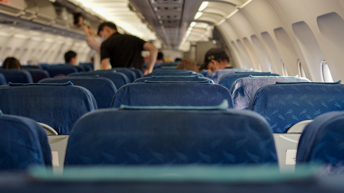 Eine Flugzeugkabine vom Sitz aus fotografiert. Einige Passagiere stehen von ihren Sitzen auf und holen ihr GepÃ¤ck aus der GepÃ¤ckablage des Flugzeugs.